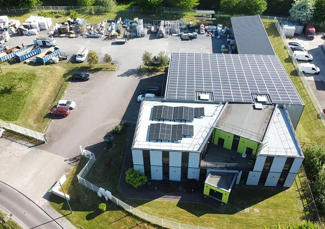 Vue aérienne du site H2RA, entreprise de couverture en Normandie, bâtiment industriel avec toiture équipée de panneaux solaires et zone de stockage.