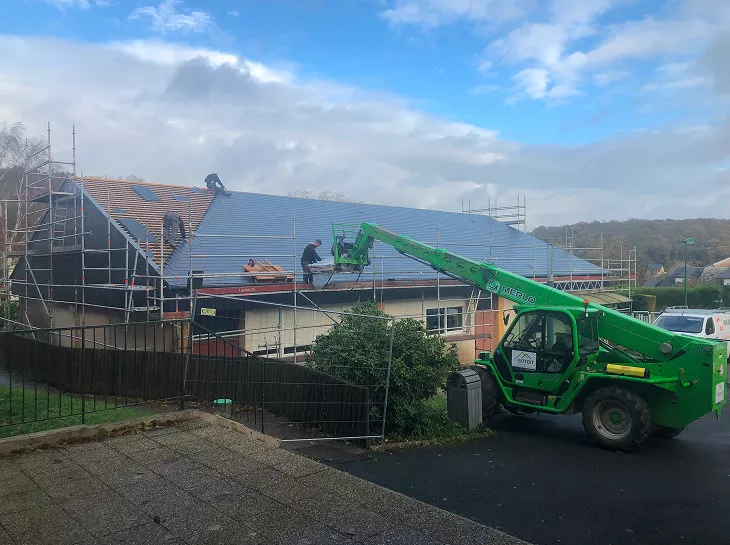 Chantier de couverture en Normandie par l’entreprise H2RA : plusieurs couvreurs posent une toiture sur un bâtiment, avec échafaudages et engin télescopique vert pour la manutention des matériaux.