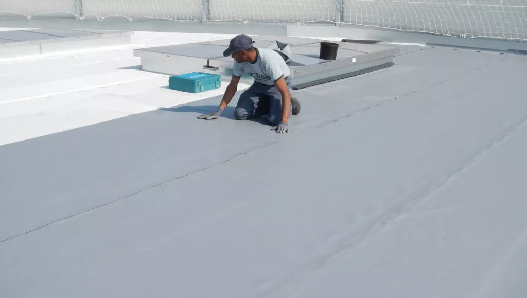 Couvreur de l’entreprise ENC à genoux sur un toit, pose d’une membrane d’étanchéité autour d’un lanterneau, chantier de couverture en Normandie.