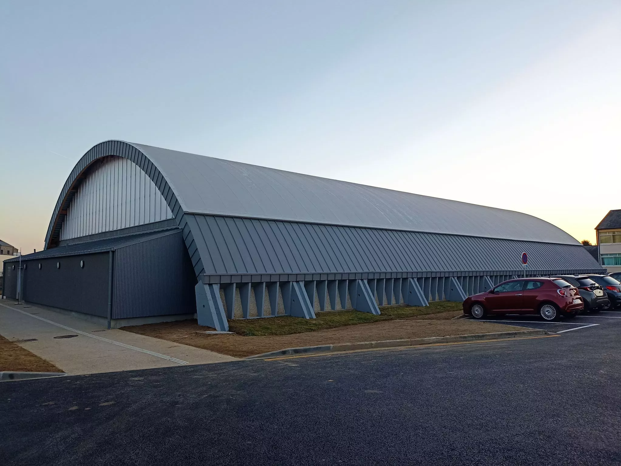 Complexe sportif avec grande toiture cintrée en bac acier gris, chantier réalisé par RENARD, entreprise couverture en Normandie.